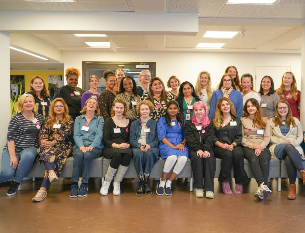 In the picture there is a large group of Neighbourhood Mothers and Neighbourhood Mother team workers. The group consists of women of different backgrounds and ages, all looking at the camera and smiling.